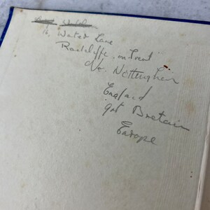 Peut inclure: Une note manuscrite sur une page blanche avec des bords bleus. La note indique une adresse : "16, Water Lane, Radcliffe on Trent, Notts, Angleterre, Grande-Bretagne, Europe."