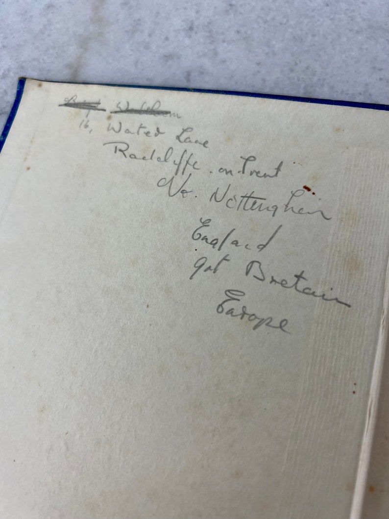 Peut inclure: Une note manuscrite sur une page blanche avec des bords bleus. La note indique une adresse : "16, Water Lane, Radcliffe on Trent, Notts, Angleterre, Grande-Bretagne, Europe."