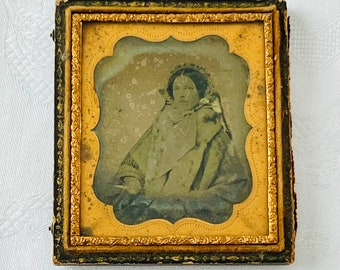 May include: A vintage photograph of a woman in a dark dress and a white shawl, framed in a gold-coloured frame with a black outer frame.