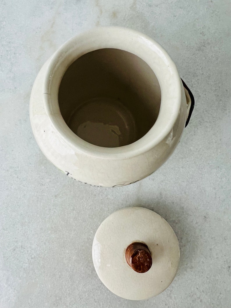 K&ouml;nnte beinhalten: Wei&szlig;e Keramikdose mit einem Holzknopf auf dem Deckel. Die Dose hat ein schlichtes Design und ist perfekt zum Aufbewahren von Kleinigkeiten.
