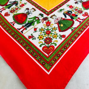 Può includere: Una sciarpa quadrata vintage con un design di arte popolare. La sciarpa presenta uno sfondo bianco con illustrazioni di persone in abiti tradizionali, fiori e cuori. Il bordo è rosso con un bordo verde e bianco e un angolo giallo.