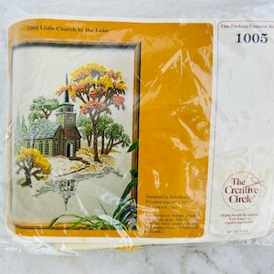 May include: A vintage embroidery kit featuring a charming scene of a small church by a lake. The kit includes a design print, fabric, yarn, and instructions. The kit is labeled "1005 Little Church by the Lake" and is from "The Creative Circle".