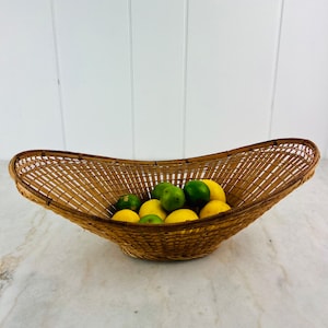 May include: A woven wicker basket in the shape of an oval with a wide, shallow bowl. The basket is filled with a mix of green limes and yellow lemons.