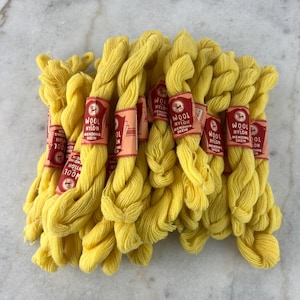 Op de afbeelding: Een stapel gele wol- en nylon herstelspoel, elk met het label "Wool & Nylon Mending Skein 100M".