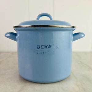 Könnte beinhalten: Hellblaue Emaille-Kochtopf mit Deckel und zwei seitlichen Griffen. Der Topf hat einen silbernen Rand und einen passenden blauen Griff am Deckel. Der Text "BEKA STAHL" ist auf der Vorderseite aufgedruckt.