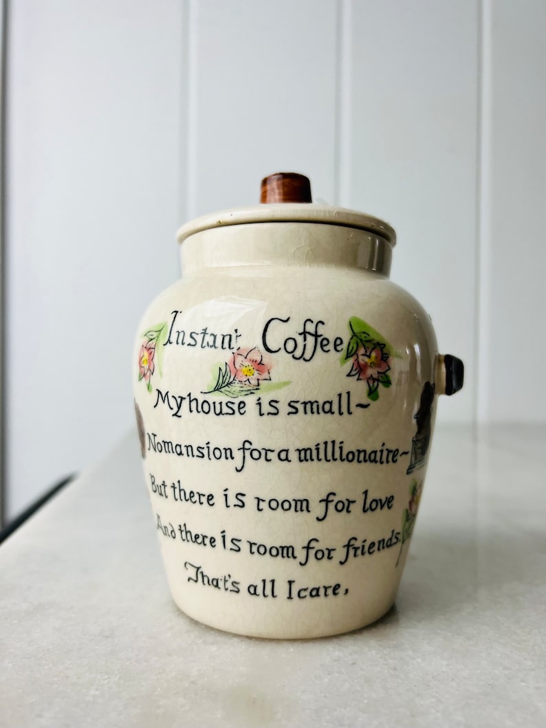 K&ouml;nnte beinhalten: Eine Kaffeedose aus Keramik mit einem Holzdeckel. Die Dose ist mit Blumen und einem handgeschriebenen Gedicht verziert, das lautet: "Instantkaffee Mein Haus ist klein - Kein Herrenhaus f&uuml;r einen Million&auml;r - Aber es gibt Platz f&uuml;r Liebe Und es gibt Platz f&uuml;r Freunde Das ist alles, was z&auml;hlt."