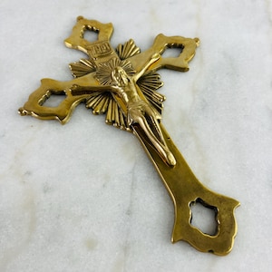Könnte beinhalten: Ein goldfarbenes Kruzifix mit einer detaillierten Darstellung von Jesus Christus. Das Kreuz weist aufwendige Details und ein Sonnenstrahlendesign hinter der Figur auf. Die Buchstaben "INRI" sind oben auf dem Kreuz zu sehen.