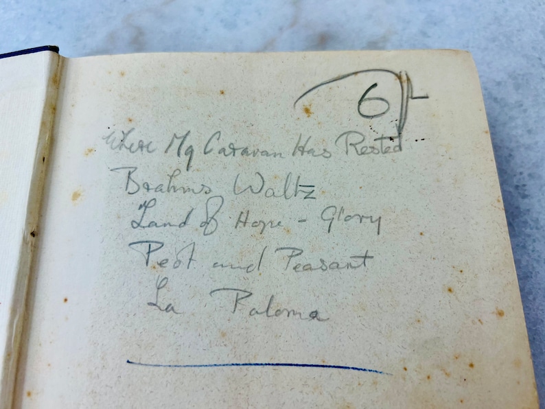 Peut inclure: Une liste de chansons manuscrites sur une page d'un livre. La liste comprend "Brahms Waltz", "Land of Hope - Glory", "Pest and Peasant", et "La Paloma".
