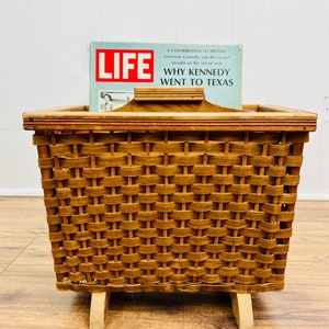May include: A woven wicker magazine basket with a wooden handle and legs. The basket is holding a copy of LIFE magazine with the headline "Why Kennedy Went to Texas".