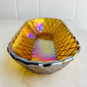 Pu&ograve; includere: Un piccolo piatto di vetro ambrato iridescente con un motivo intrecciato. Il piatto ha un bordo argentato.