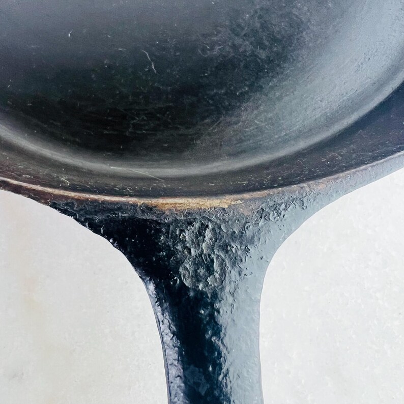 May include: Close-up of a well-worn, black cast iron skillet. The handle has a textured, rough surface, while the cooking surface is smooth. The skillet shows signs of use and age, with a dark, seasoned finish. The handle curves downward.