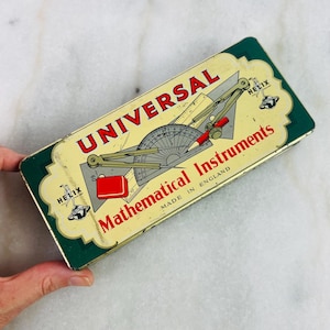 May include: Vintage rectangular tin box labeled "UNIVERSAL Mathematical Instruments MADE IN ENGLAND." The box features a green border and a cream-colored center with illustrations of drafting tools. The text is in red and black.