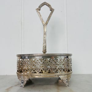May include: Silver serving dish with a decorative handle. The dish features an openwork design around the sides and rests on ornate feet. The handle is V-shaped with decorative detailing.
