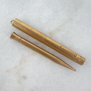 Puede incluir: Un juego de pluma estilográfica y lápiz mecánico a juego de color dorado. La pluma tiene un capuchón y un clip. El lápiz tiene una punta puntiaguda.