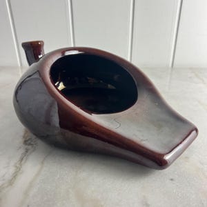 May include: A dark brown ceramic chamber pot with a spout. The pot has a smooth, glossy finish.