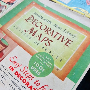 May include: Close-up of a vintage book cover titled "Hammond's Decorative Maps." The cover features a green and orange color scheme with the text in red and black. A green circle states "A wide choice of sizes, colors, subjects for 1001 uses."