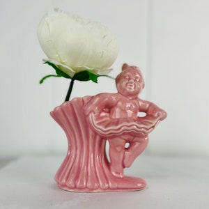 May include: A pink ceramic ballerina figurine vase with a white flower.