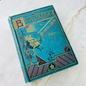Könnte beinhalten: Ein blaugrünes Buch mit goldener Beschriftung mit dem Titel "Encyclopedic of Business & Social Forms". Der Einband zeigt ein dekoratives Design mit einer Frau in einem fließenden Kleid, Blumen und geometrischen Mustern.