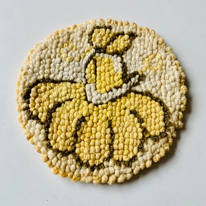 Op de afbeelding: Een rond, geel en bruin vloerkleed met een bloemenpatroon. Het vloerkleed is gemaakt van garen en heeft een textuur.