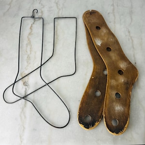 May include: A pair of dark metal wire sock forms with a top hook and a pair of wooden sock forms featuring a smooth, light brown finish with multiple circular cutouts throughout the structure, designed for shaping and drying hosiery items.