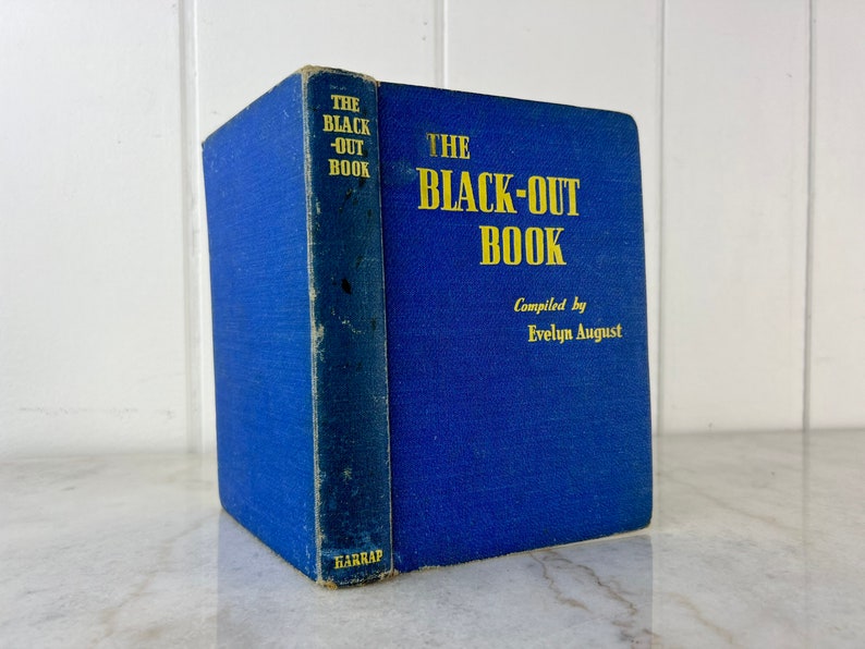 Peut inclure: Un livre reli&eacute; de couleur bleue intitul&eacute; "The Black-Out Book" compil&eacute; par Evelyn August. Le livre est pos&eacute; sur une surface blanche.