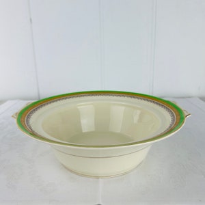 May include: A white ceramic serving bowl with a green and gold rim. The bowl has two handles on the sides.