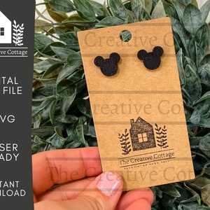 May include: A brown card with the text "The Creative Cottage" and a small house illustration. Two black wooden Mickey Mouse ears are attached to the card.