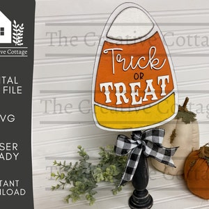 May include: A wooden cutout of a candy corn with the text "Trick or Treat" in white. The cutout is on a black pedestal with a black and white checkered bow. The cutout is surrounded by fall decor, including two pumpkins.