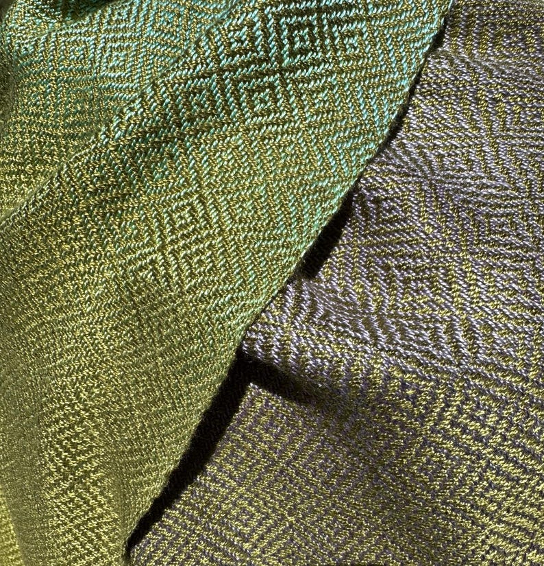 May include: Two pieces of fabric with a geometric pattern woven into the material. One piece is a green and gold colour, and the other is a purple and gold colour.