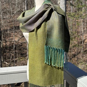 May include: A green and blue woven scarf with a fringe. The scarf is draped over a mannequin.
