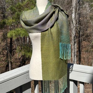 May include: A green and purple woven scarf with a geometric pattern and teal fringe.