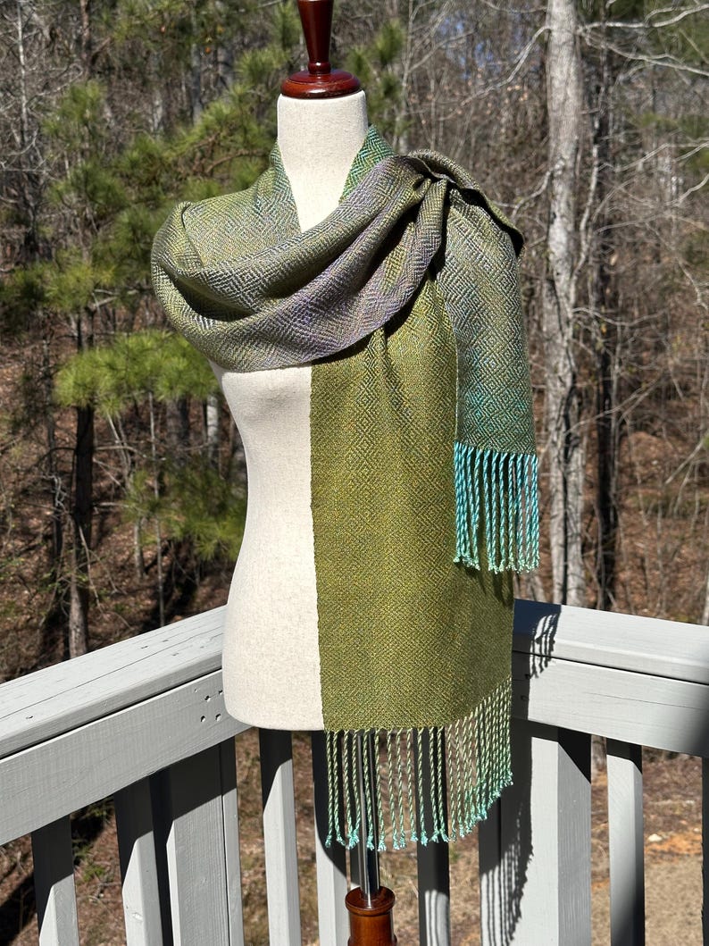 May include: A green and purple woven scarf with a geometric pattern and teal fringe.