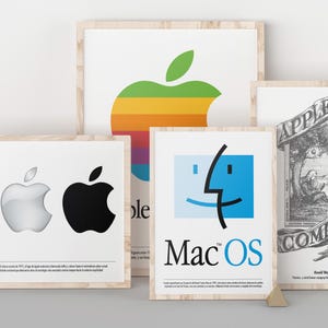 May include: Four framed prints featuring Apple branding. One shows a rainbow, silver, and black apple logo. Another displays a large rainbow apple. A third features the blue Mac OS logo. The fourth is a black and white illustration of Isaac Newton.