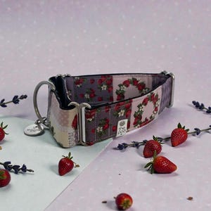 May include: A dog collar with a strawberry pattern. The collar features a patchwork design with various strawberry and floral prints in shades of pink, red, and gray. It has a silver metal clasp and a small tag.