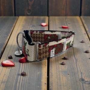 May include: A dog collar with a strawberry and diamond pattern. The collar has a silver metal clasp and a small tag. The collar is on a wooden surface with strawberry slices and chocolate chips.