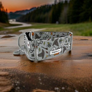 May include: A gray and white dog collar with a whimsical pattern featuring glasses, hats, and other magical objects. The collar has a silver buckle and a silver D-ring. The text "thepod.me" is printed on the collar.