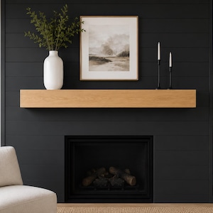 May include: A rectangular light oak wood fireplace mantel shelf mounted horizontally on a black shiplap wall above a fireplace insert. The mantel features a visible natural wood grain pattern and a smooth, flat top surface for display items.