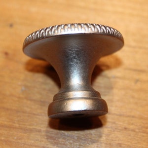 May include: A silver cabinet knob with a decorative, raised, circular edge.