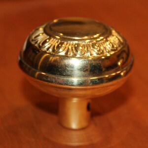 May include: A gold-toned door knob with a decorative, ornate design around the edge.