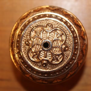 May include: A gold-colored metal bottle stopper with an intricate design. The stopper has a small hole in the center.