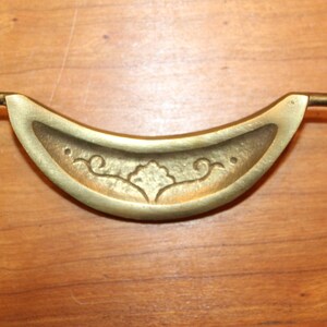 May include: A brass drawer pull with a crescent shape and a decorative floral design.
