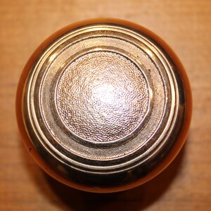 May include: A round, polished brass door knob with concentric circles and a textured center.