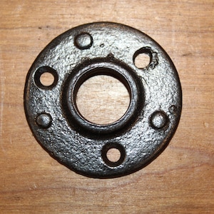 May include: Black metal pipe flange with four holes around the edge and a center hole. The flange is designed to connect pipes and fittings.
