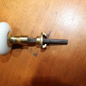 May include: A white porcelain door knob with a brass base and a threaded metal spindle.