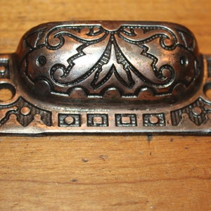 May include: A silver-toned metal drawer pull with an ornate design. The pull has a rectangular base with a curved top and a floral pattern.