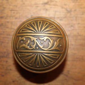 May include: A brass door knob with a decorative floral design and a sunburst pattern.