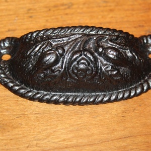 May include: Black cast iron drawer pull with a rope edge and floral design.