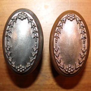 May include: Two oval-shaped door knobs with a decorative floral design. One knob is silver and the other is copper.