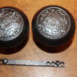 May include: Two black door knobs with a silver floral design and a silver metal door latch.