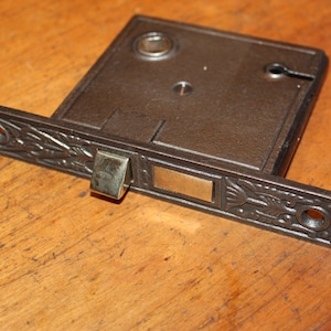 May include: A vintage, cast iron door latch with a decorative floral design. The latch has a brass lever and a keyhole.
